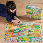 Child playing with a dinosaur-themed puzzle on a wooden floor, with a matching puzzle box in the background.