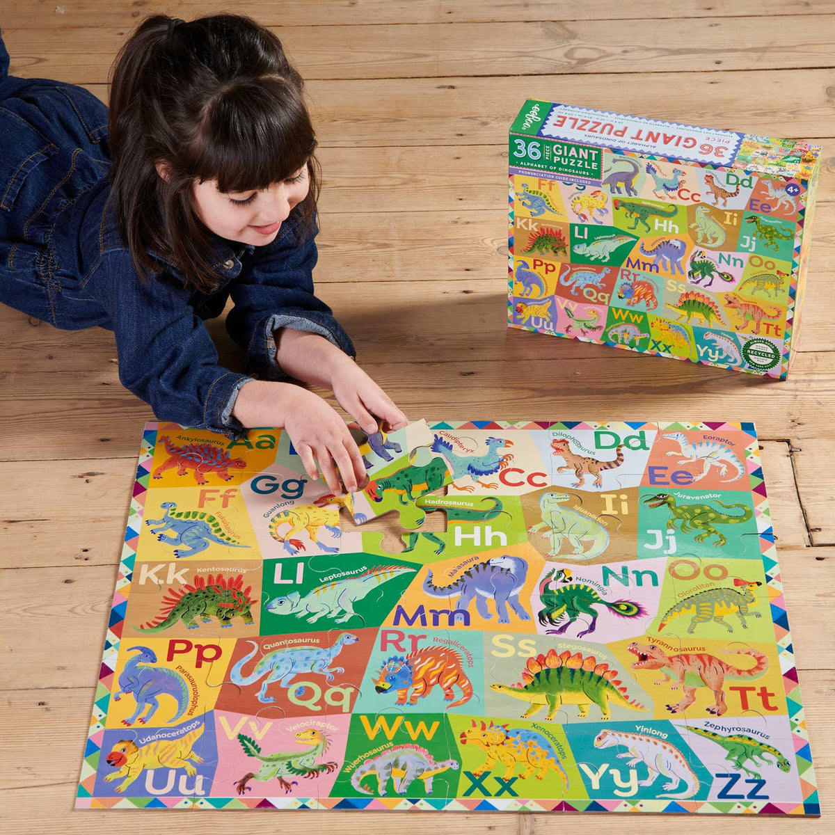 Child playing with a dinosaur-themed puzzle on a wooden floor, with a matching puzzle box in the background.