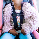Child in a car seat wearing a fluffy pink jacket, holding an unbuckling device.