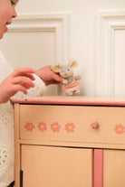 Child holding a toy mouse next to a pink dresser with floral decals.