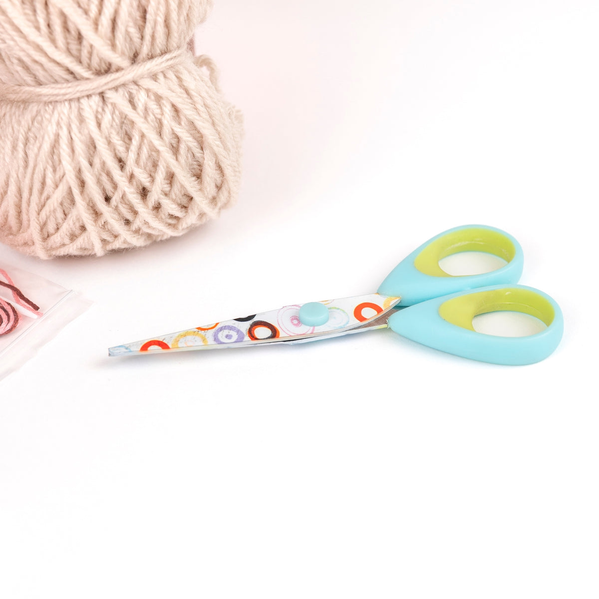 Colorful scissors with patterned handles next to a ball of yarn on a white background