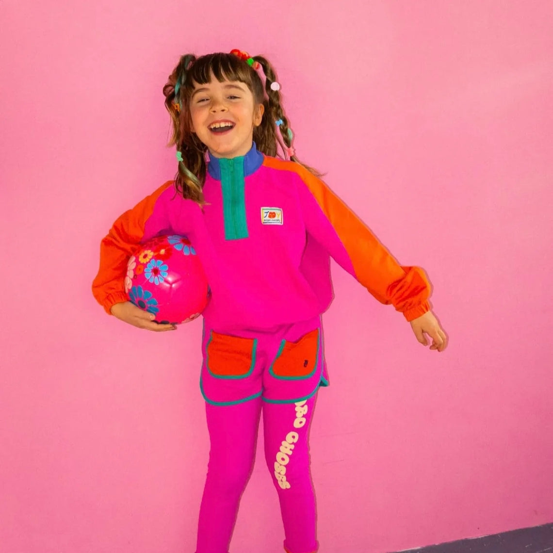 Child wearing a colorful outfit with a pink background