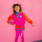 Child wearing a colorful outfit with a pink background