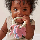 Baby holding a silicone teether with butterfly designs.