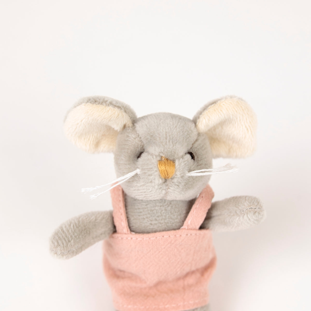 A plush mouse toy with gray fur, cream-colored ears, a small yellow stitched nose, and white whiskers, wearing pink overalls against a plain white background.