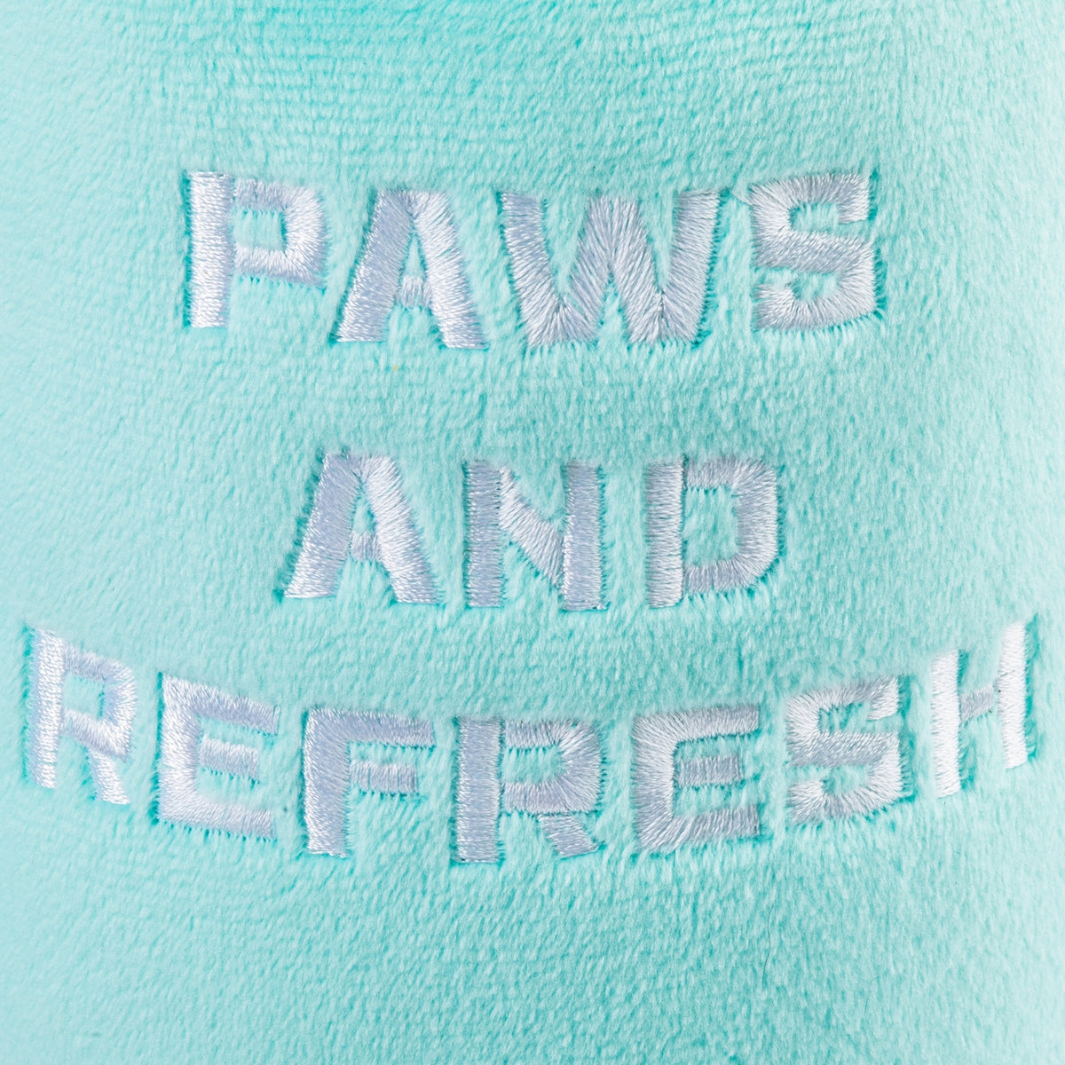 A close-up of a mint green plush fabric with white embroidered text reading 'PAWS AND REFRESH'.