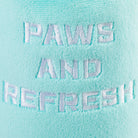 A close-up of a mint green plush fabric with white embroidered text reading 'PAWS AND REFRESH'.