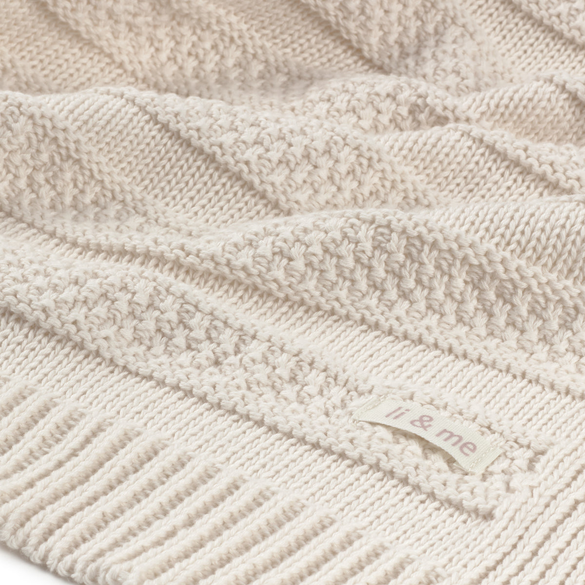 Close-up of a textured beige knitted blanket with 'it & me' branding.