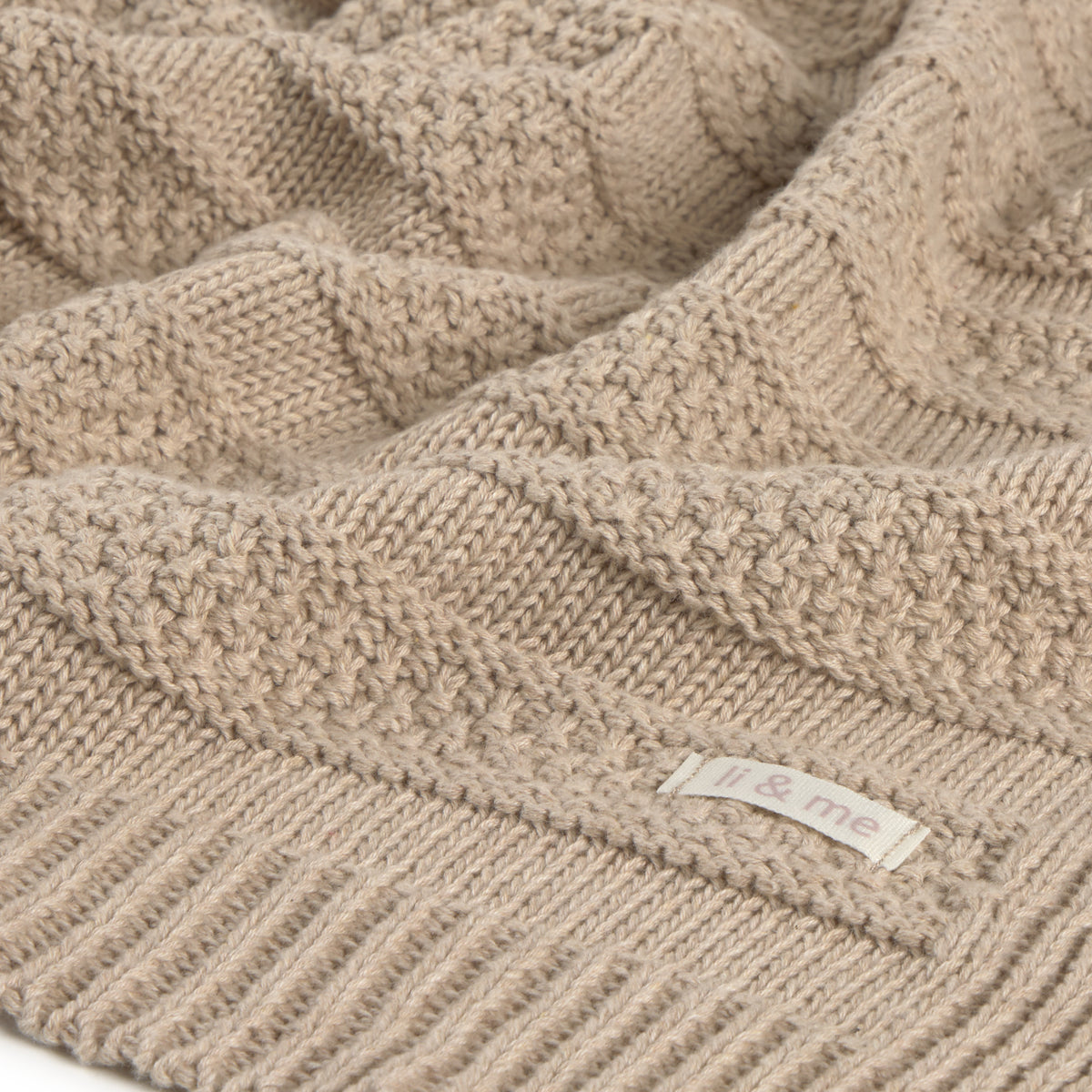 Close-up of a beige knitted blanket with a brand label.