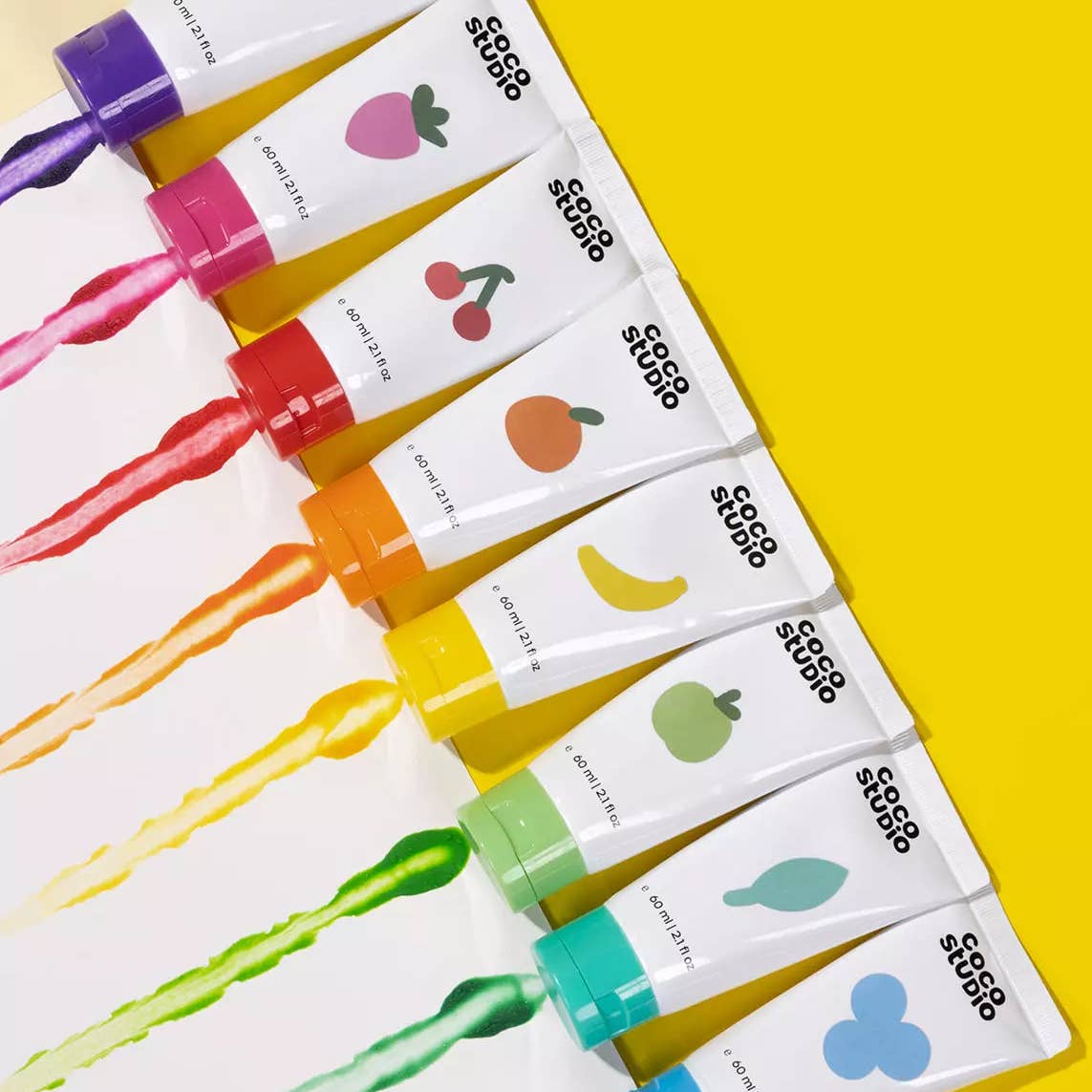 Eight white paint tubes with colorful fruit illustrations and black '$$$$$' text, arranged diagonally on a bright yellow background with corresponding paint splashes visible.