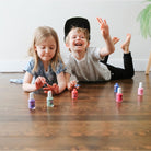 Two children playing with small bottles on a wooden floor.