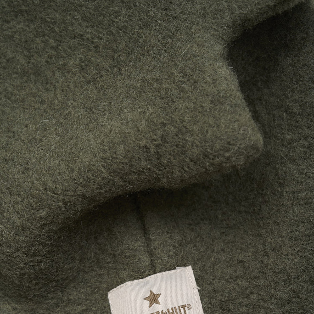 Close-up of dark green fabric with a brand label featuring a star emblem.