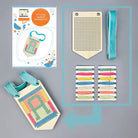 Cross-stitch banner decoration kit with pattern guide, wooden grid, fabric strips, and completed banner on a gray background.