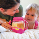 Woman and child with a pink sippy cup filled with a yellow liquid on a white blanket.