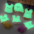 Several small plush bunny-shaped keychain or bag charms glow in the dark, shown in different colors including mint green, yellow, pink, and purple. Some are displayed alone, and one is attached to a chain.