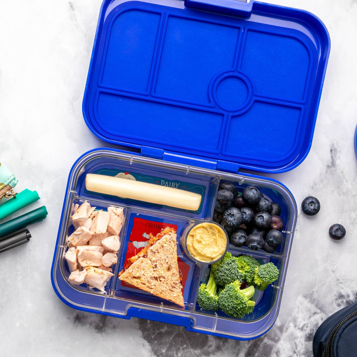 Blue bento box with compartments containing food items on a marble surface