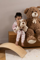 Child holding a teddy bear next to a large teddy bear on a wooden surface.