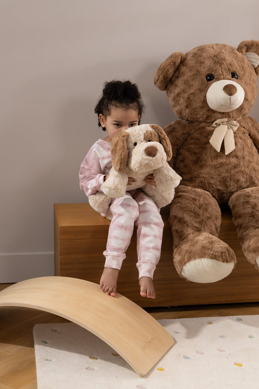 Child holding a teddy bear next to a large teddy bear on a wooden surface.