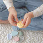 Child's hands holding a yellow object with pastel-colored items on a textured surface