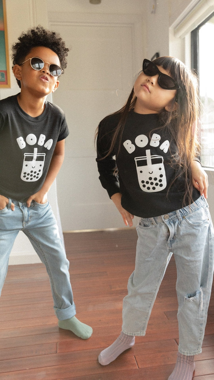 Two children wearing black t-shirts with a bubble tea graphic and sunglasses indoors.