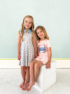 Two young girls posing together on a white block against a light blue wall.