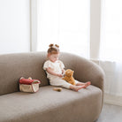 Child sitting on a beige sofa with toys in a bright room
