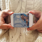 Hands holding a 'BFF Friendship Bracelet Kit' tin against a knitted fabric background