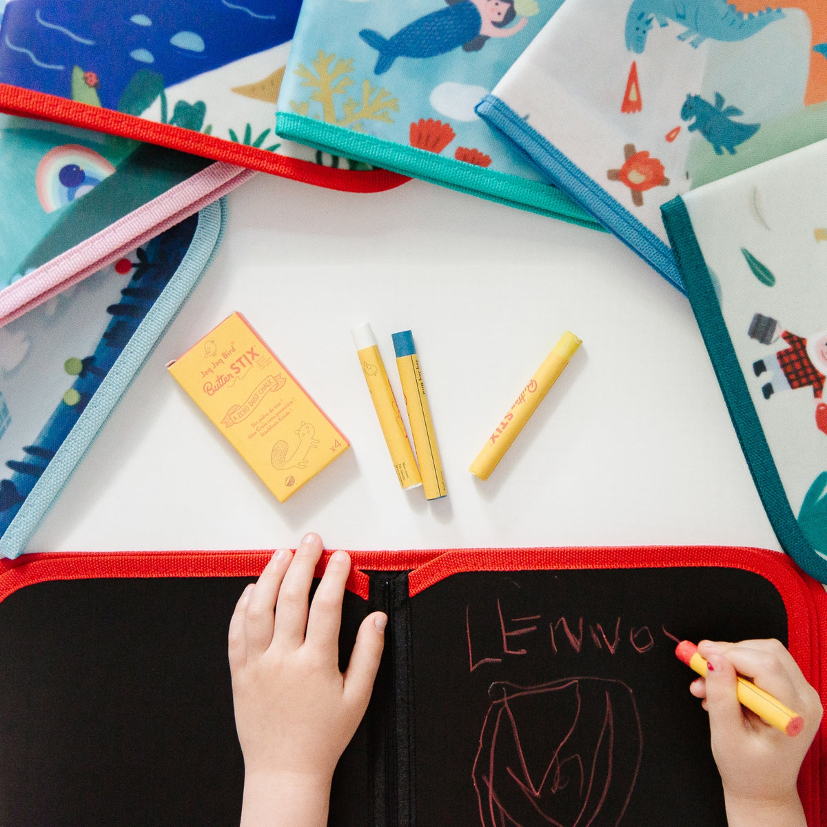 Colorful children's art supplies including markers and drawing books on a white surface.