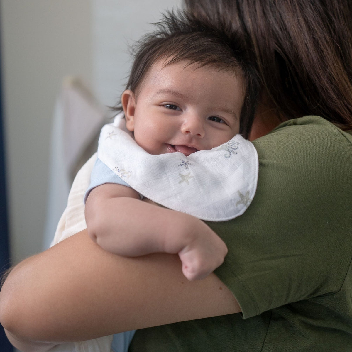 Baby wearing a white bib with embroidered designs, held by an adult in a green shirt.