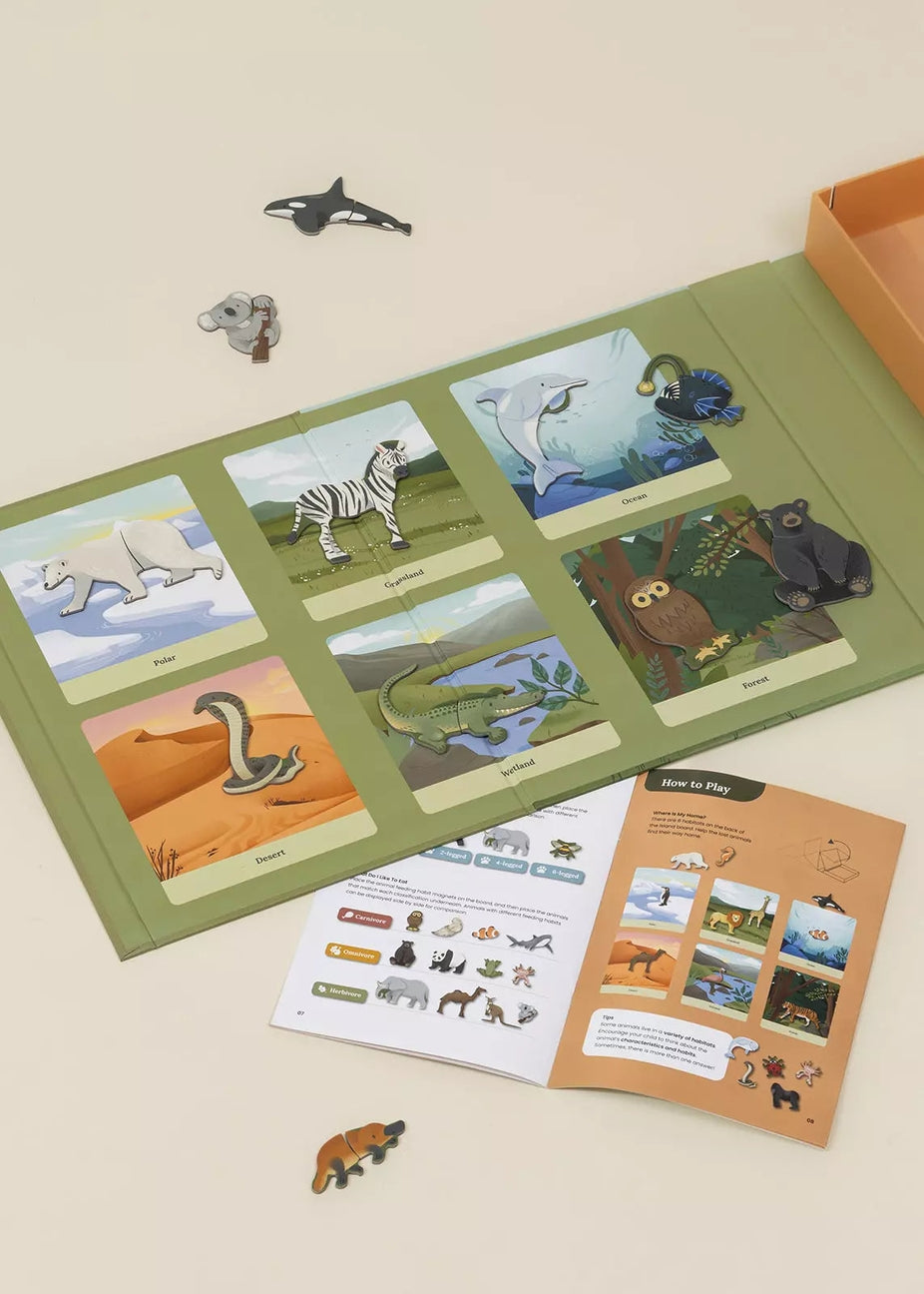 An educational animal-themed activity kit laid out on a light beige surface, featuring a green folder with illustrated animal cards, an instruction booklet, and several small animal cutout pieces.