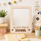Wooden plaque with 'my first day of school' text on a desk with school supplies.