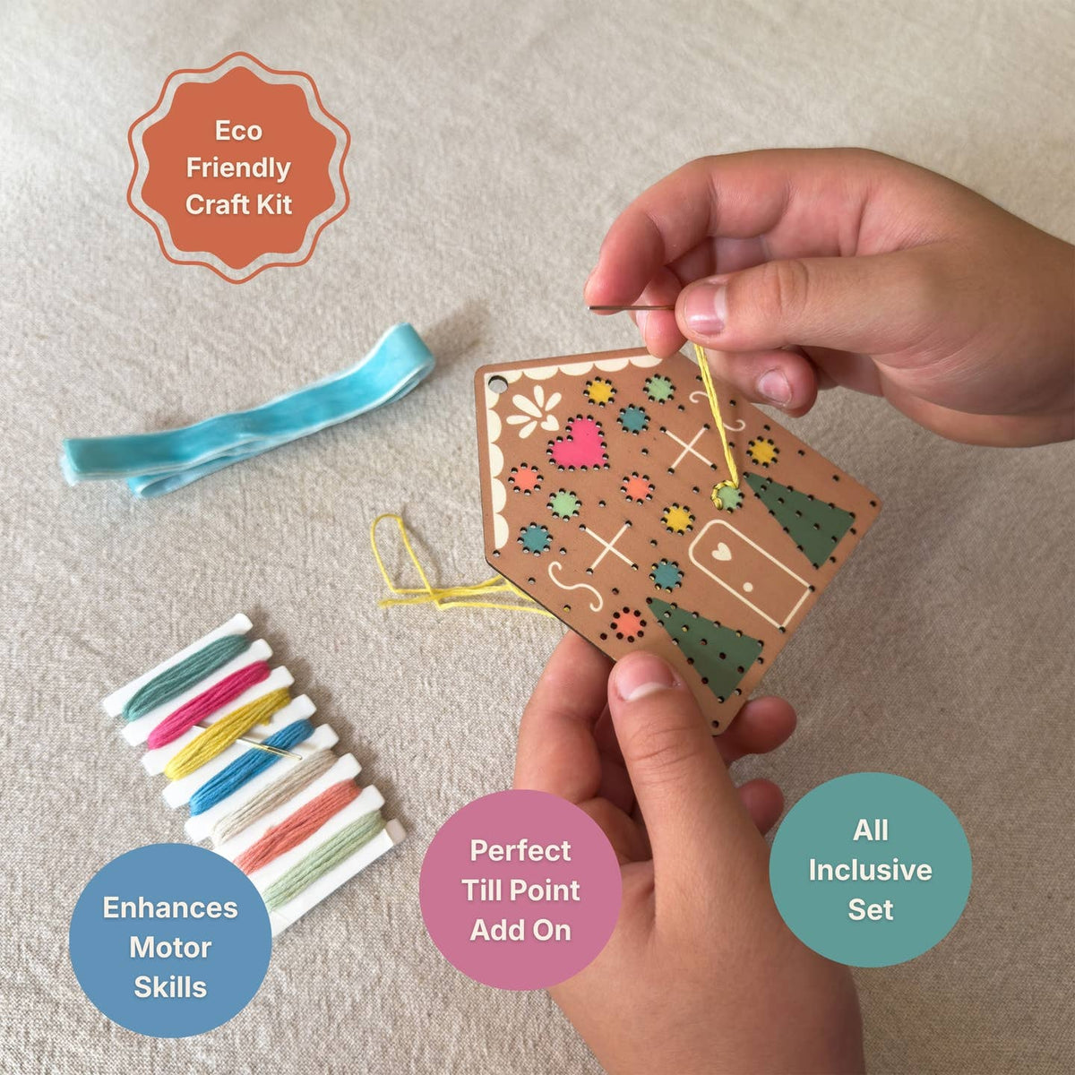 A hands-on craft kit shown on a light beige fabric surface, with a person's hands holding a wooden bird-shaped craft piece and threading it. Surrounding items include a blue ribbon, a row of colorful thread spools, and text callouts reading 'Eco Friendly Craft Kit,' 'Enhances Motor Skills,' 'Perfect Till Point Add On,' and 'All Inclusive Set.