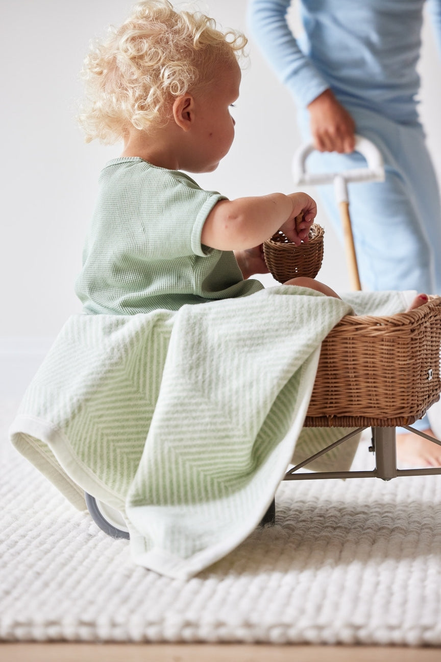 Child playing with a woven basket on a white blanket