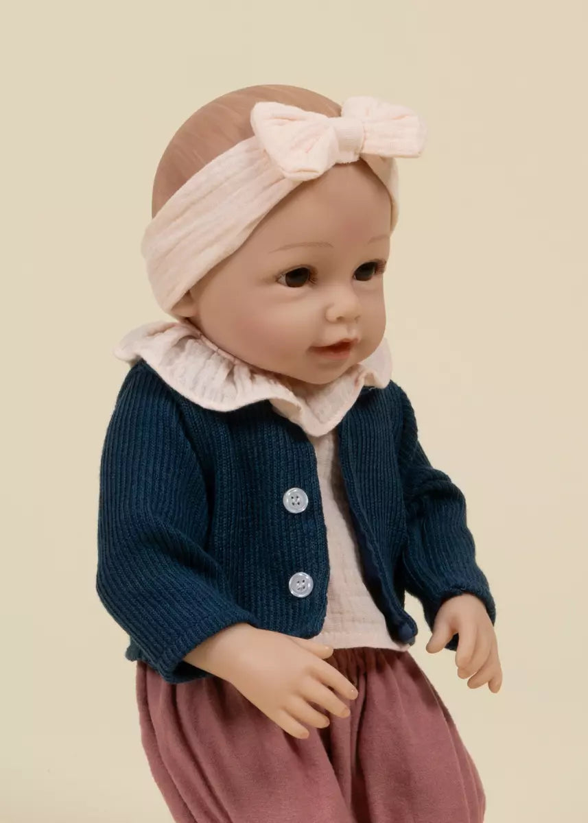 Doll wearing a navy blue cardigan, pink headband, and pink pants on a beige background
