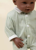 Baby wearing a green and white striped onesie on a beige background