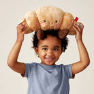 Child holding a plush toy resembling a croissant above their head against a plain background