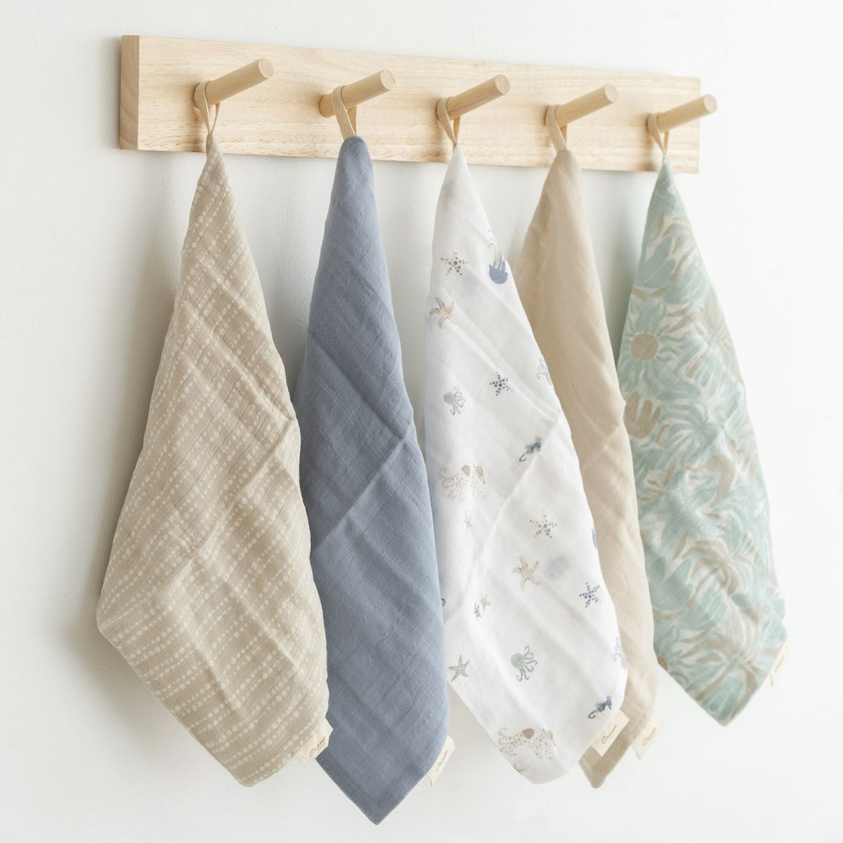 Set of five baby swaddle blankets hanging on a wooden rack against a white background