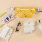 Yellow pouch with cartoon design, sunglasses, and other items on a beige background