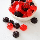 Gummy berries in red and black on a white surface with a bowl of gummy berries.