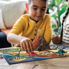 Child playing with a dinosaur-themed board game on a wooden table.