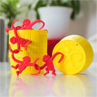 Red plastic monkeys linked together on and around a yellow plastic storage barrel and its matching lid for the Barrel of Monkeys Game by Continuum Games.