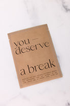 Kraft paper product packaging with 'you deserve a break' text on a marble surface