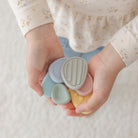 Hands holding four small, colorful objects against a neutral background