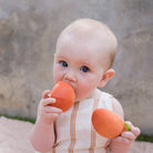 Baby holding and playing with orange toys against a neutral background
