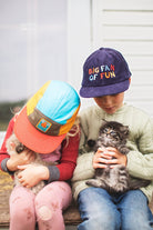 Two children wearing colorful hats holding kittens outdoors.