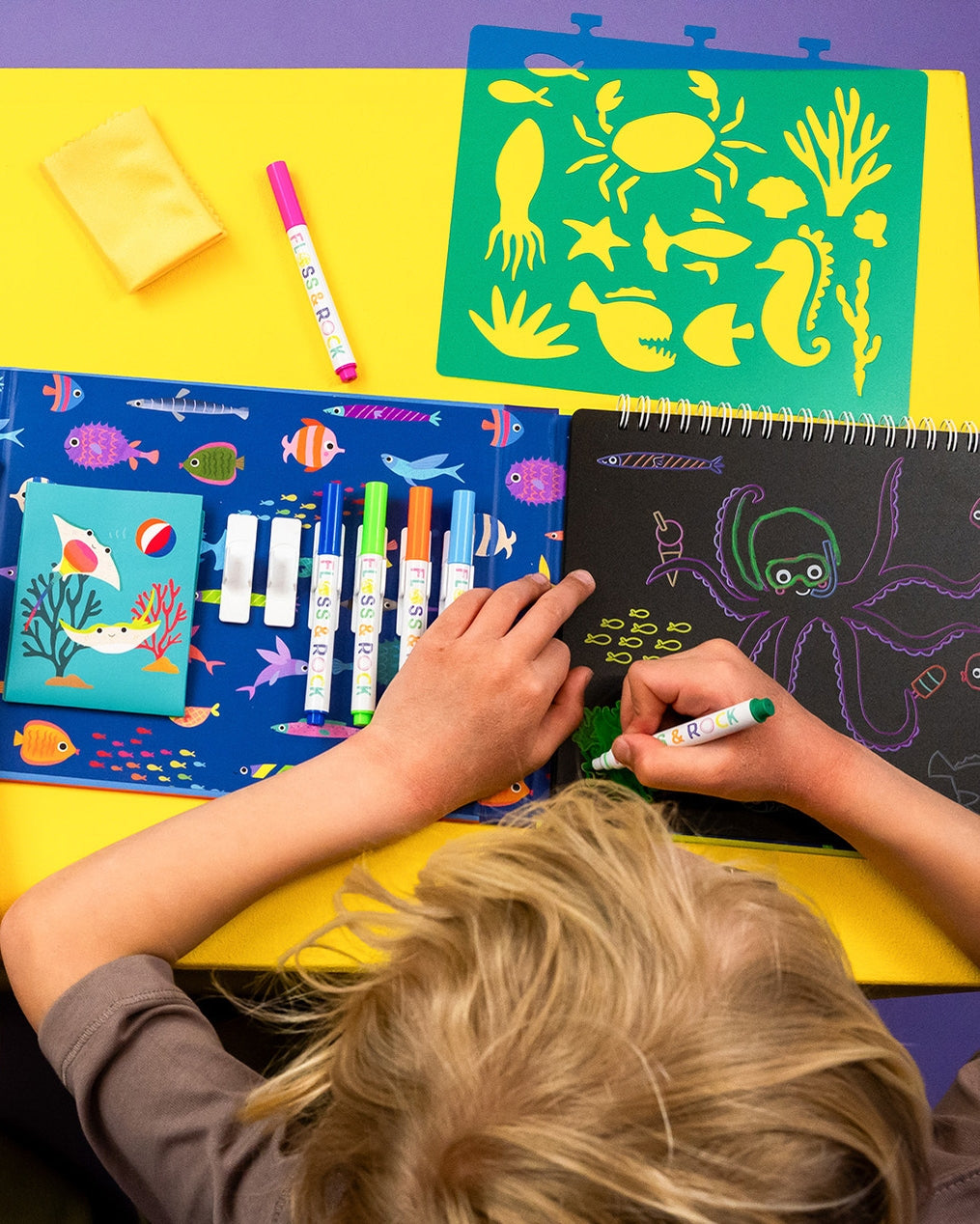 Child drawing with markers on a colorful table with art supplies