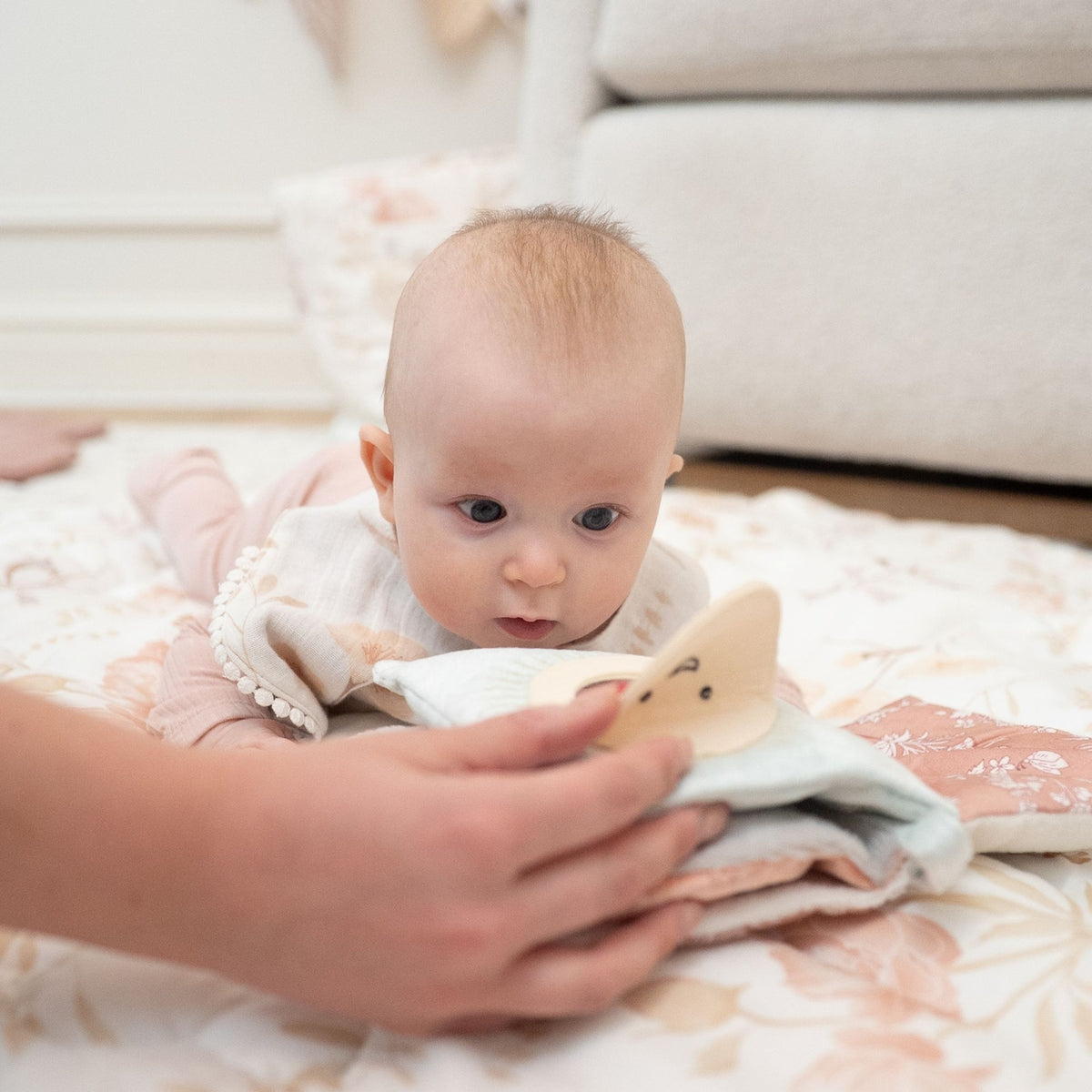 Baby lying on a blanket with a person's hand holding a book