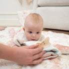 Baby lying on a blanket with a person's hand holding a book