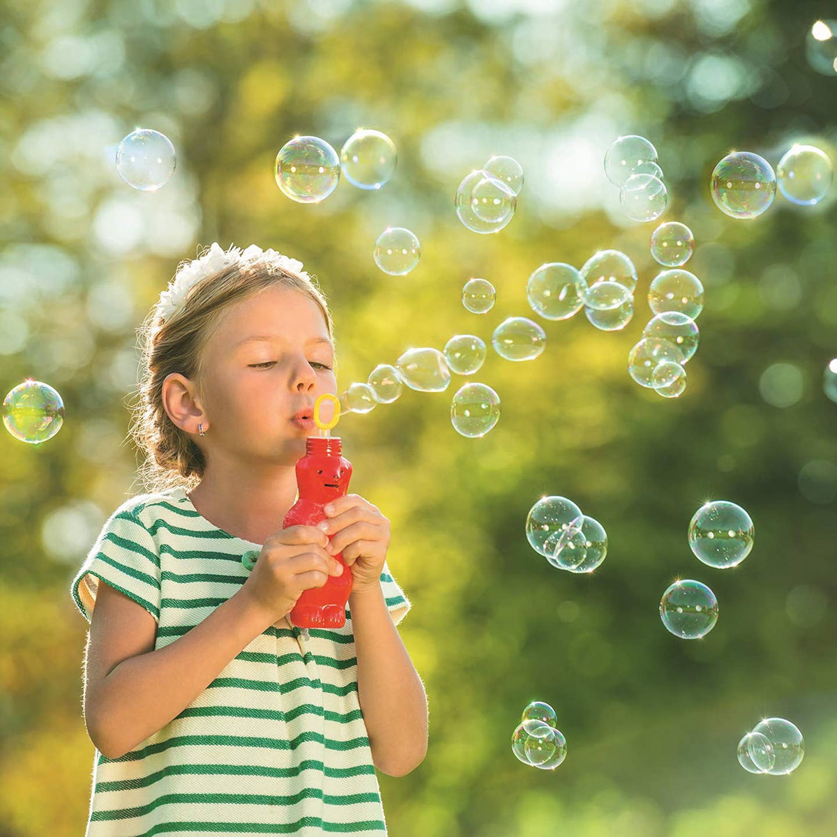 Child blowing bubbles outdoors with a blurred green background