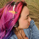 Person with colorful hair wearing headphones, sitting in a grassy area.